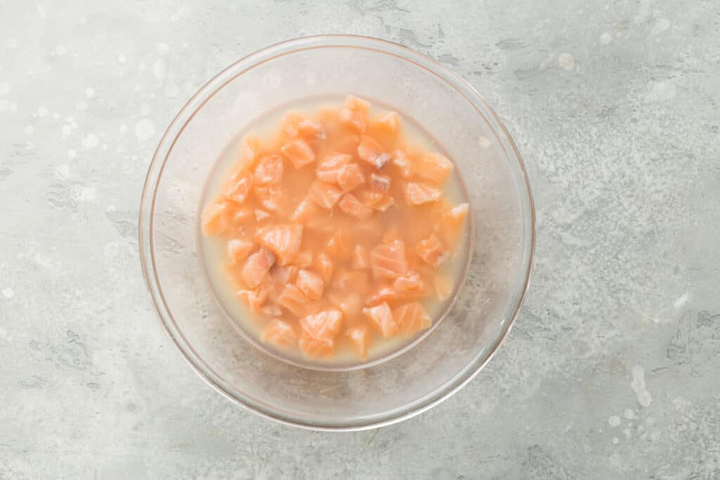 Recipiente transparente con salmón en trozos y jugo de cítricos.