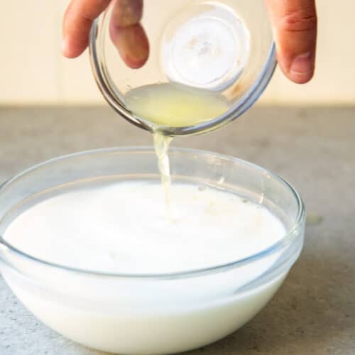 Una mano vertiendo jugo de limón en un recipiente hondo de vidrio con leche