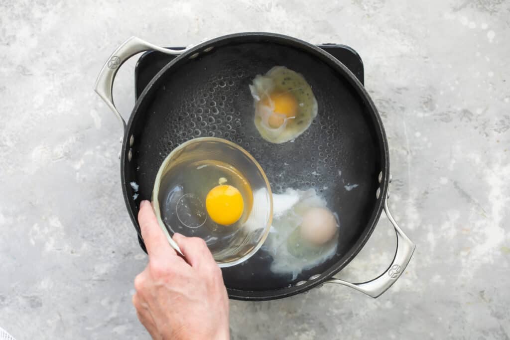Una olla con agua hirviendo al momento de depositar el huevo crudo del recipiente individual para escalfarlo