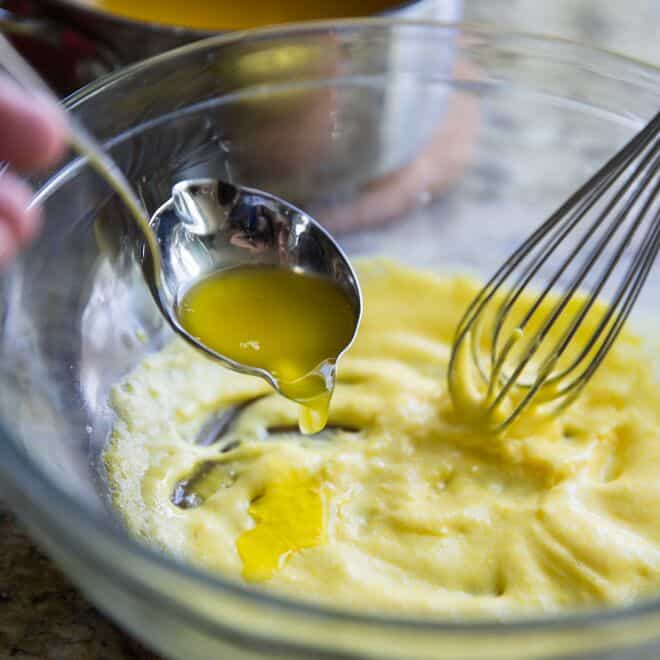 Añadiendo con una cuchara gota a gota la mantequilla clarificada a la mezcla de yemas de huevo para hacer salsa holandesa