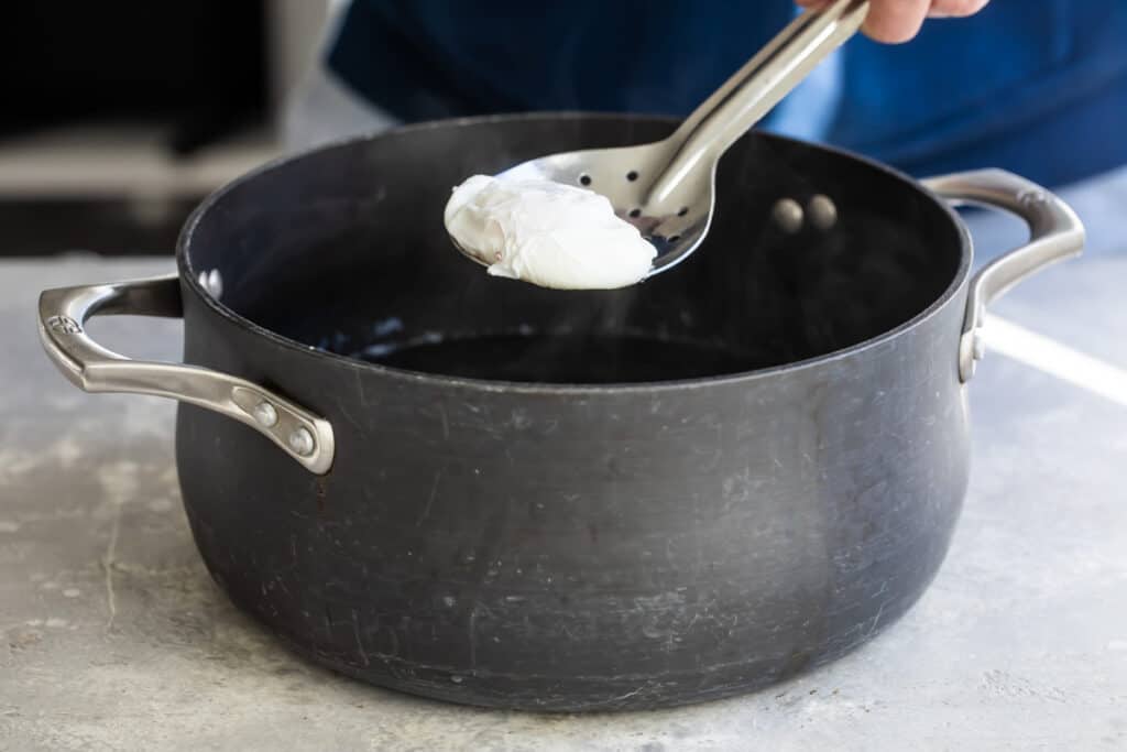 Cuchara espumadera sacando un huevo escalfado ya cocido de la olla 