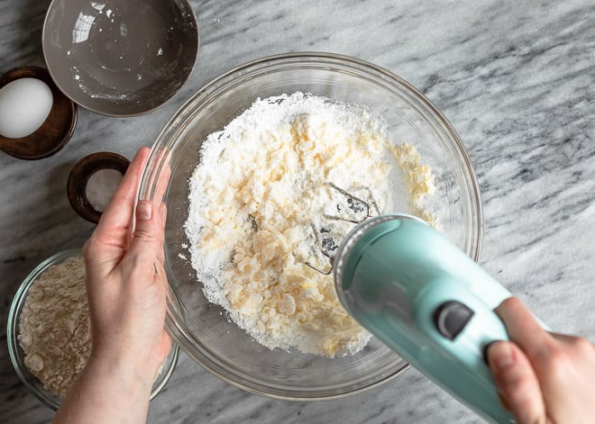 Mezclando harina en la mezcla para pasta de base de tarta con batidora eléctrica de mano en recipiente hondo