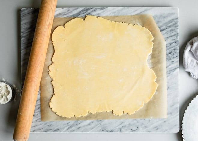 Pasta para base de tarta extendida con rodillo de madera sobre papel encerado