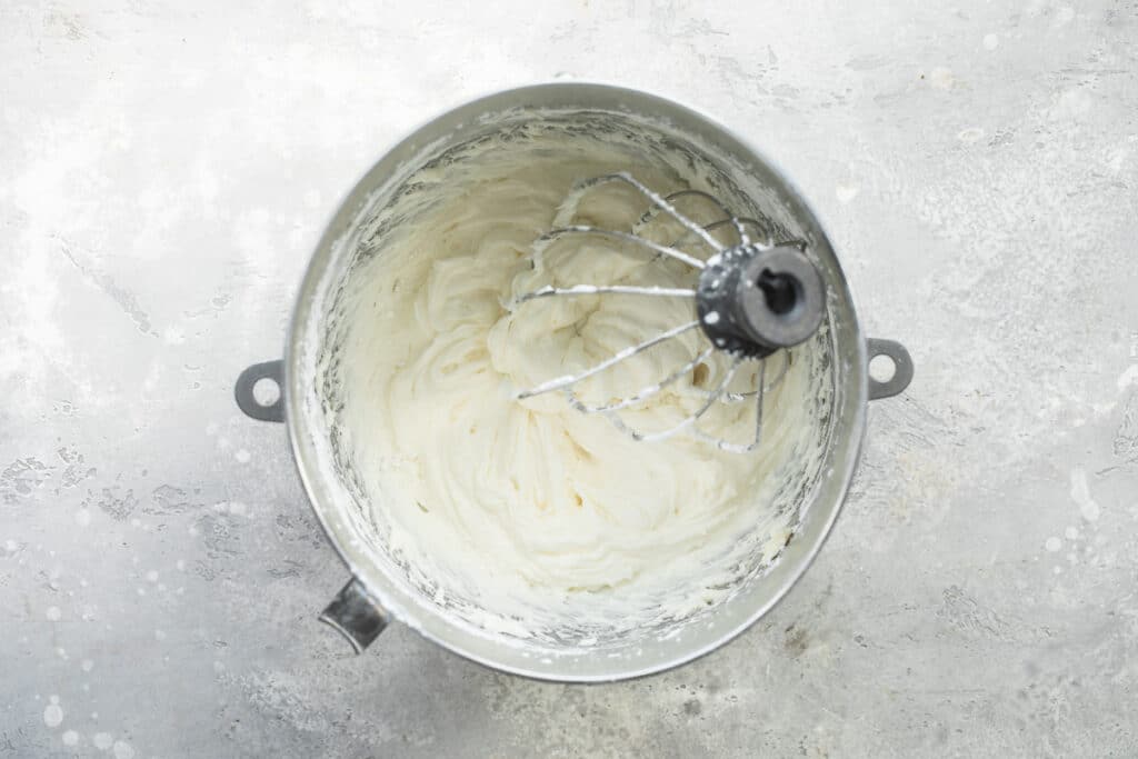 Batiendo la cubierta de queso crema con globo de batir en un recipiente hondo de metal