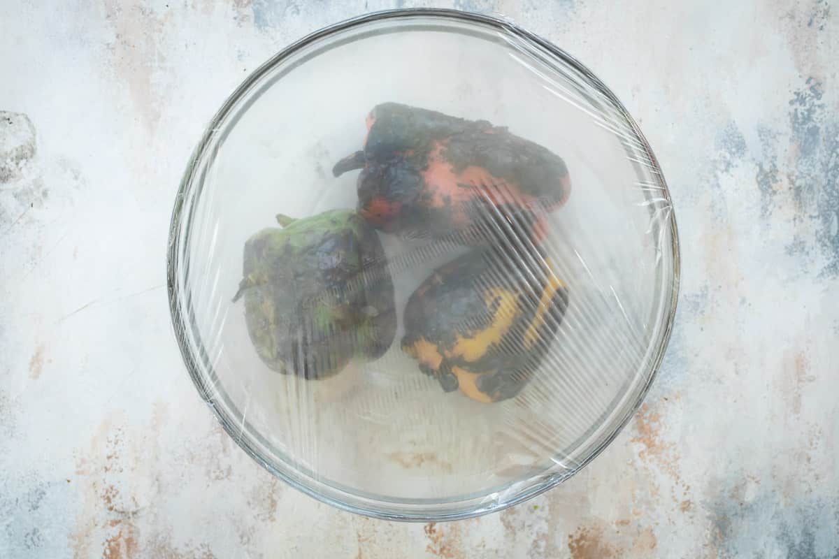 Pimientos asados en un recipiente hondo cubierto con plástico de cocina para guardar el vapor