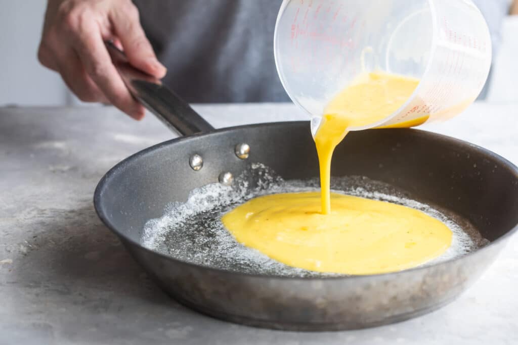 Vertiendo la mezcla de huevo en el sartén con mantequilla