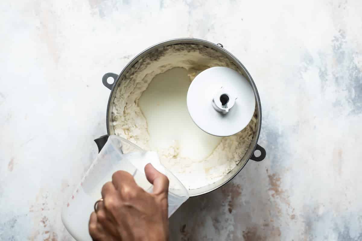 Añadiendo leche a la mezcla de harina en el recipiente de la batidora fija