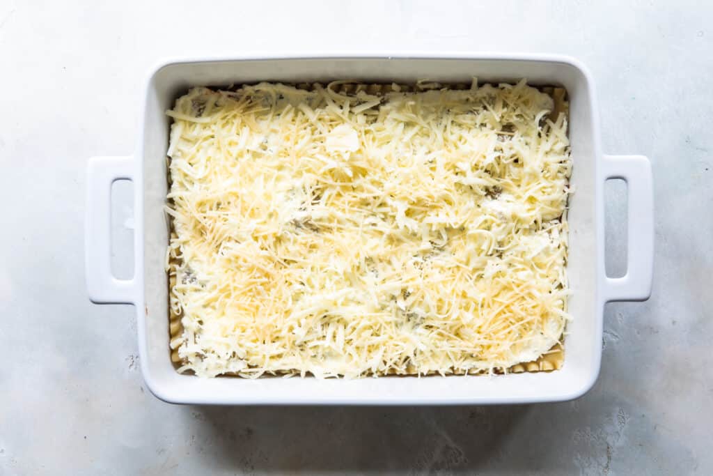 Capa de pasta de lasagna cubierta con la mezcla de ricotta y queso Parmesano y mozzarella rallados
