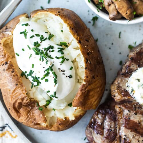 Una patata al horno junto a un bistec.