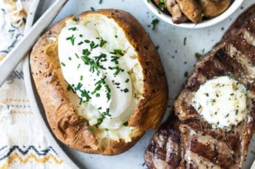 Una patata al horno junto a un bistec.