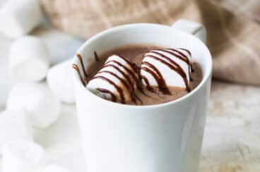 Chocolate caliente con malvaviscos y jarabe de chocolate para adornar servido en una taza blanca de cerámica