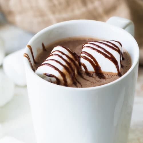 Chocolate caliente con malvaviscos y jarabe de chocolate para adornar servido en una taza blanca de cerámica