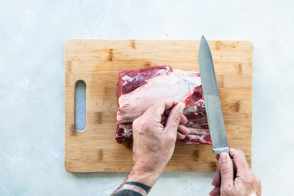 Levantando la parte grasa del lomo de res crudo para separarla y cortarla con el cuchillo