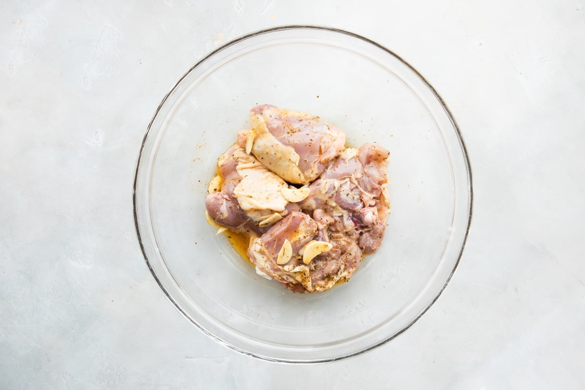 Muslos de pollo crudos en un recipiente hondo de vidrio con los ingredientes para marinar