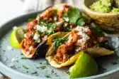 Tacos al pastor servidos con con cebolla, cilantro y limón, con guacamole por un lado
