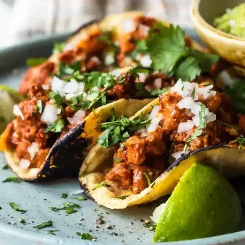 Tacos al pastor servidos con con cebolla, cilantro y limón, con guacamole por un lado