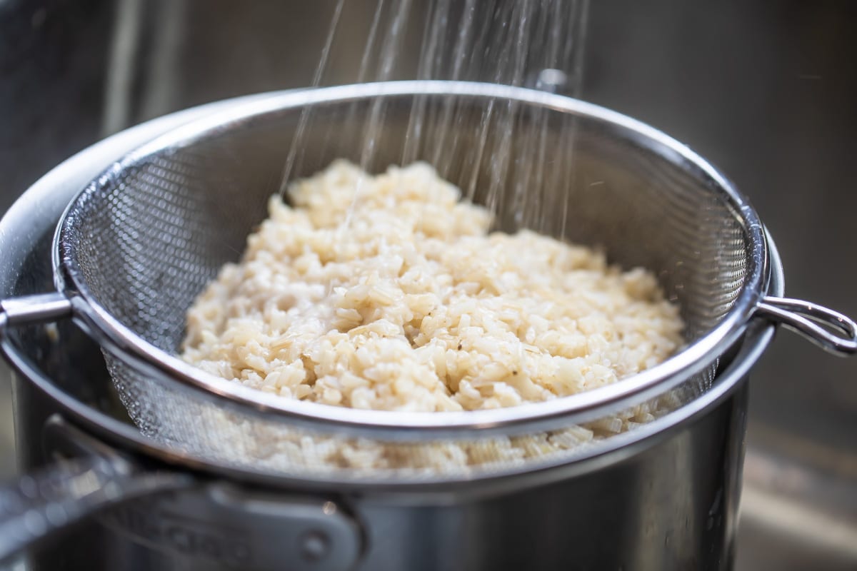 Enjuagando con agua tibia el arroz integral ya cocido y vertido en el colador