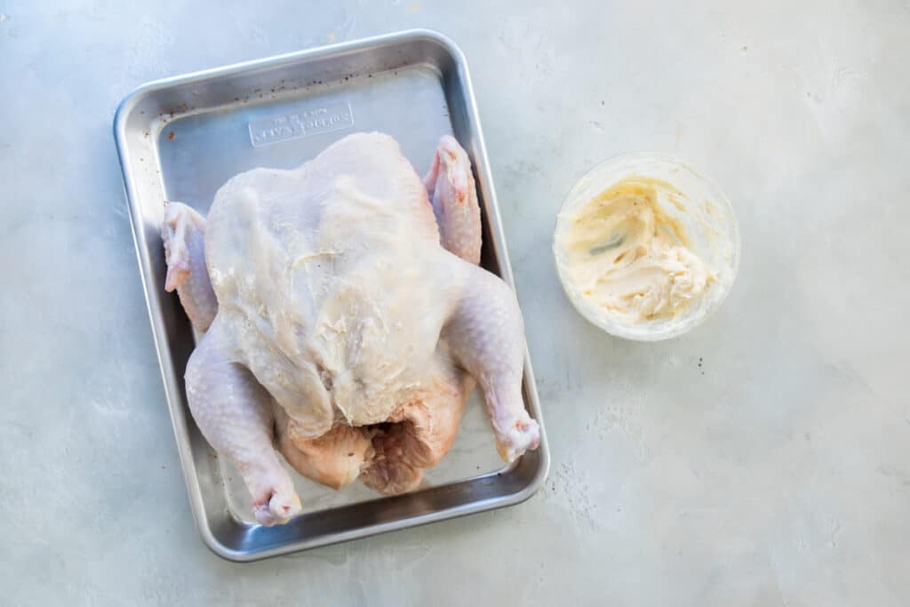 Pollo entero, crudo, sobre una charola, untado con la mezcla de mantequilla.