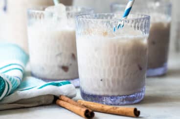 Tres vasos transparente con agua de horchata adornados con ramas de canela