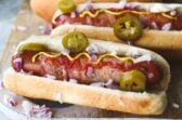 Hot dogs con tocino servidos con mostaza, mayonesa, catsup, cebolla y rodajas de chile jalapeño en conserva